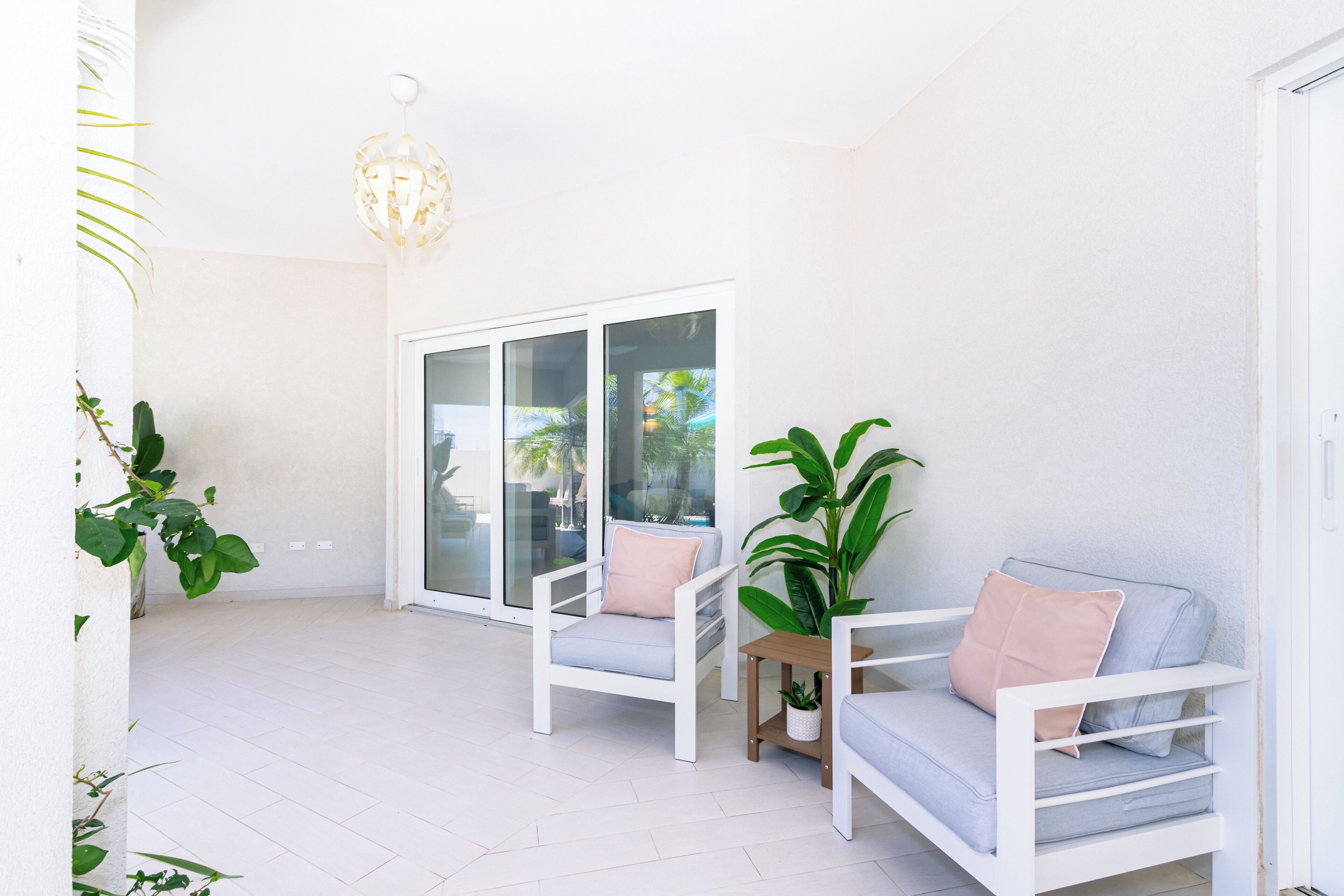 A bright, airy patio with white furniture and a large sliding glass door leading to a pool area.