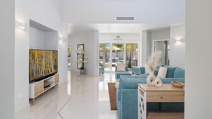 Ein modernes Wohnzimmer mit Flachbildfernseher, einem blauen Sofa, einem Holztisch und einer weißen Konsole.