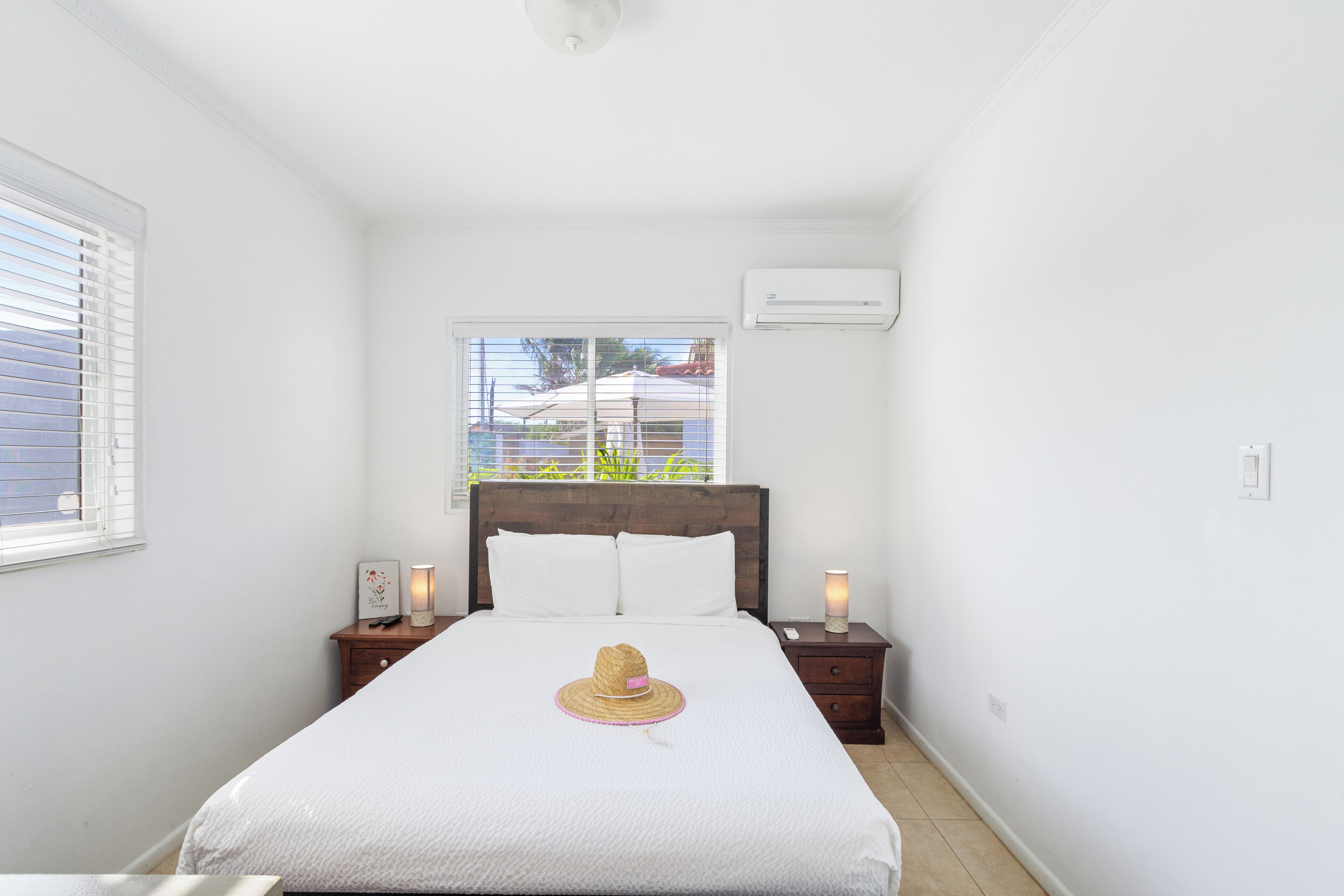 A neatly arranged bedroom with a bed, bedside lamps, a nightstand, and a window with blinds.