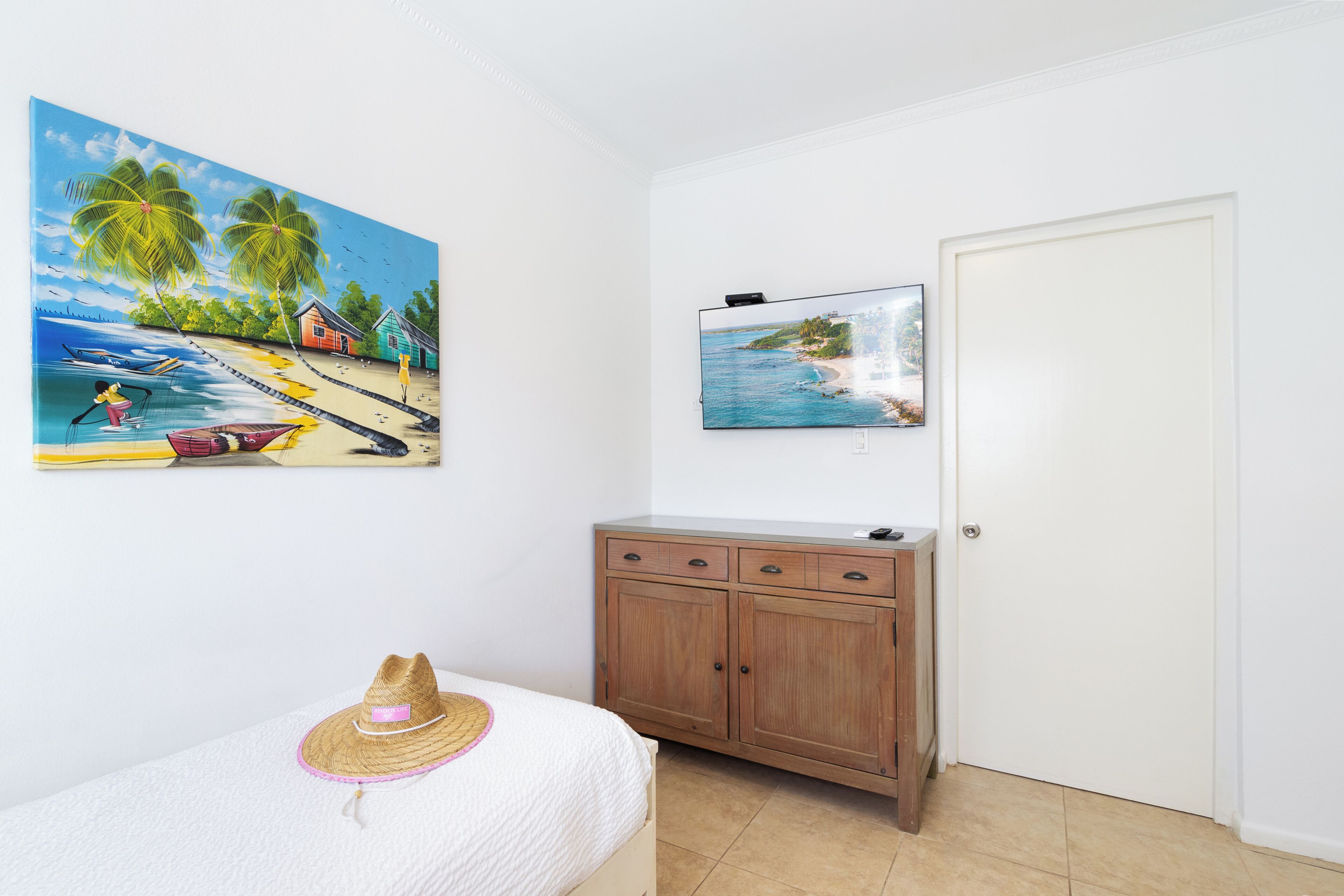 A bedroom with a bed, a wooden cabinet, a door, and two paintings on the wall.