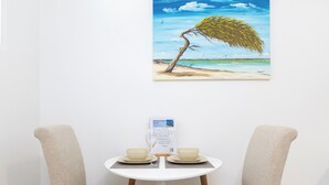 A dining table with two chairs, a menu, and a painting of a beach scene. - Little Paradise #5 - Barica Geel (Noord)