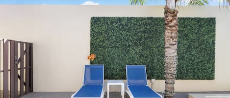 Een zwembadgedeelte met twee blauwe ligbedden, een tafeltje en een decoratieve plant.
