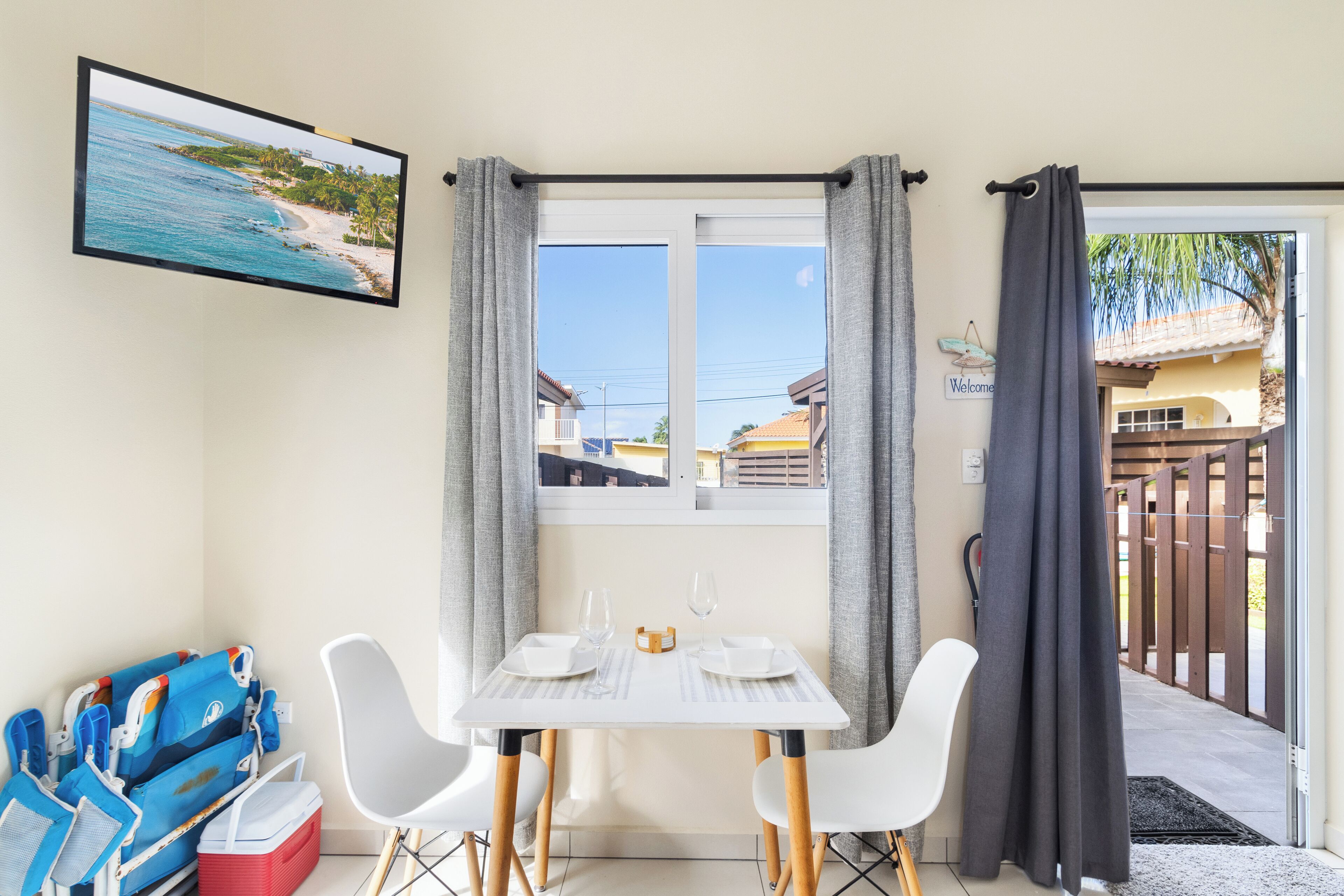 A room with a table set for two, a television on the wall, and a view of a beach through a window.
