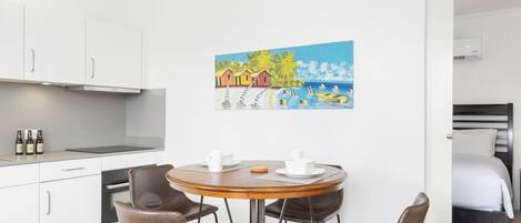Eine moderne Küche mit weißen Schränken, einem Esstisch mit vier Stühlen und einem Bild einer Strandansicht an der Wand.