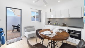 A modern kitchen with white cabinets, a built-in oven, and a dining area with a round table and chairs. - Little Paradise #1 - Prikichi (Noord)