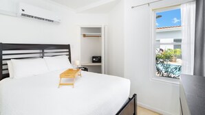 A bedroom with a bed, bedside table, and a window with a view of a swimming pool. - Little Paradise #1 - Prikichi (Noord)
