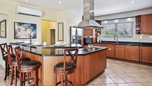 A modern kitchen with a central island, bar stools, stainless steel appliances, and wooden cabinets. - Kamay 85 (Noord)
