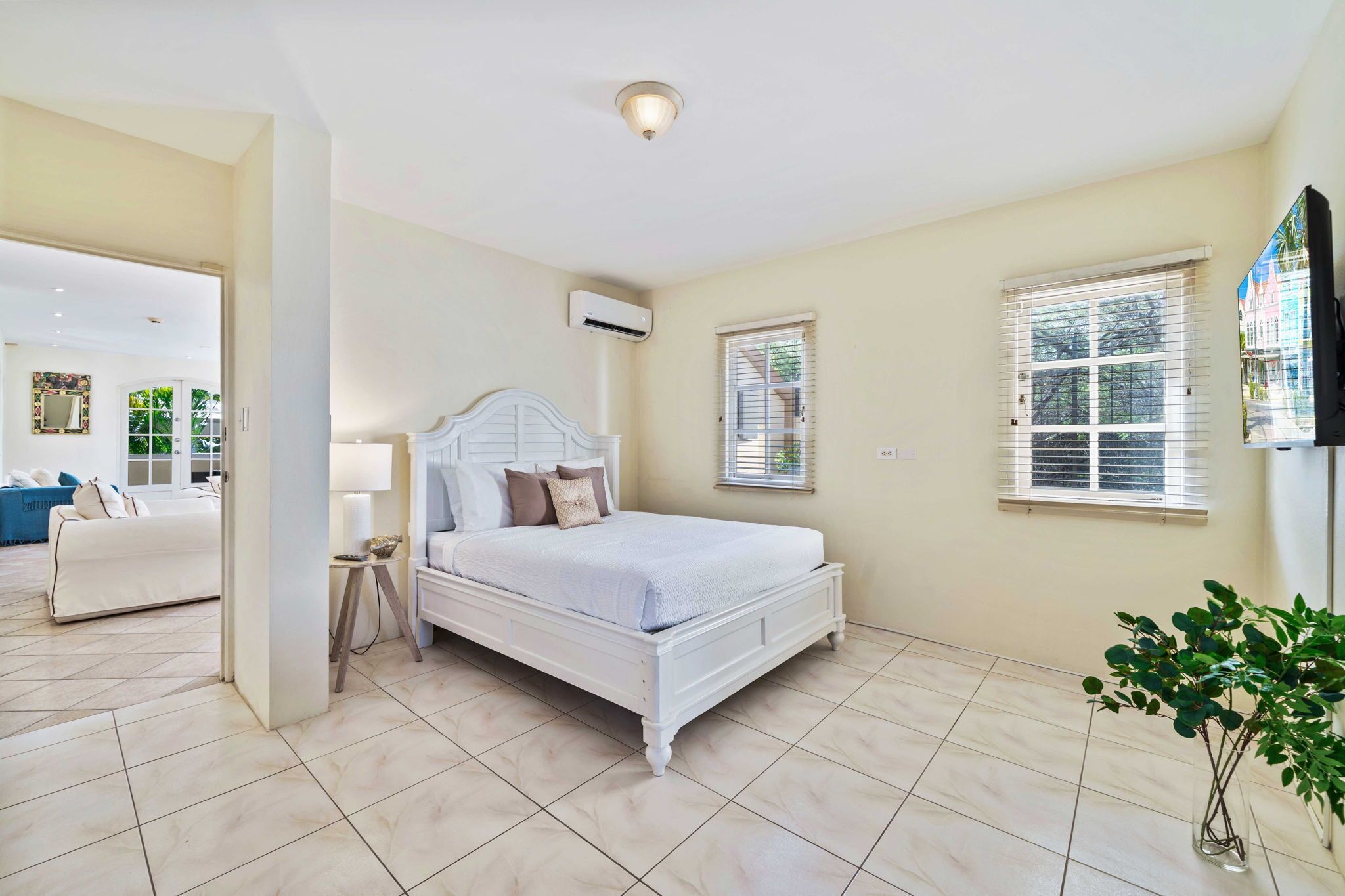 A bedroom with a white bed, a bedside table, a lamp, and a potted plant.
