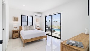 A modern bedroom with a large bed, bedside tables, a nightstand, and a view of a swimming pool. - Tanki Leendert 43-k (Oranjestad)