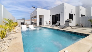 A modern pool area with a clear blue pool, white walls, and a few lounge chairs. - Tanki Leendert 43-k (Oranjestad)