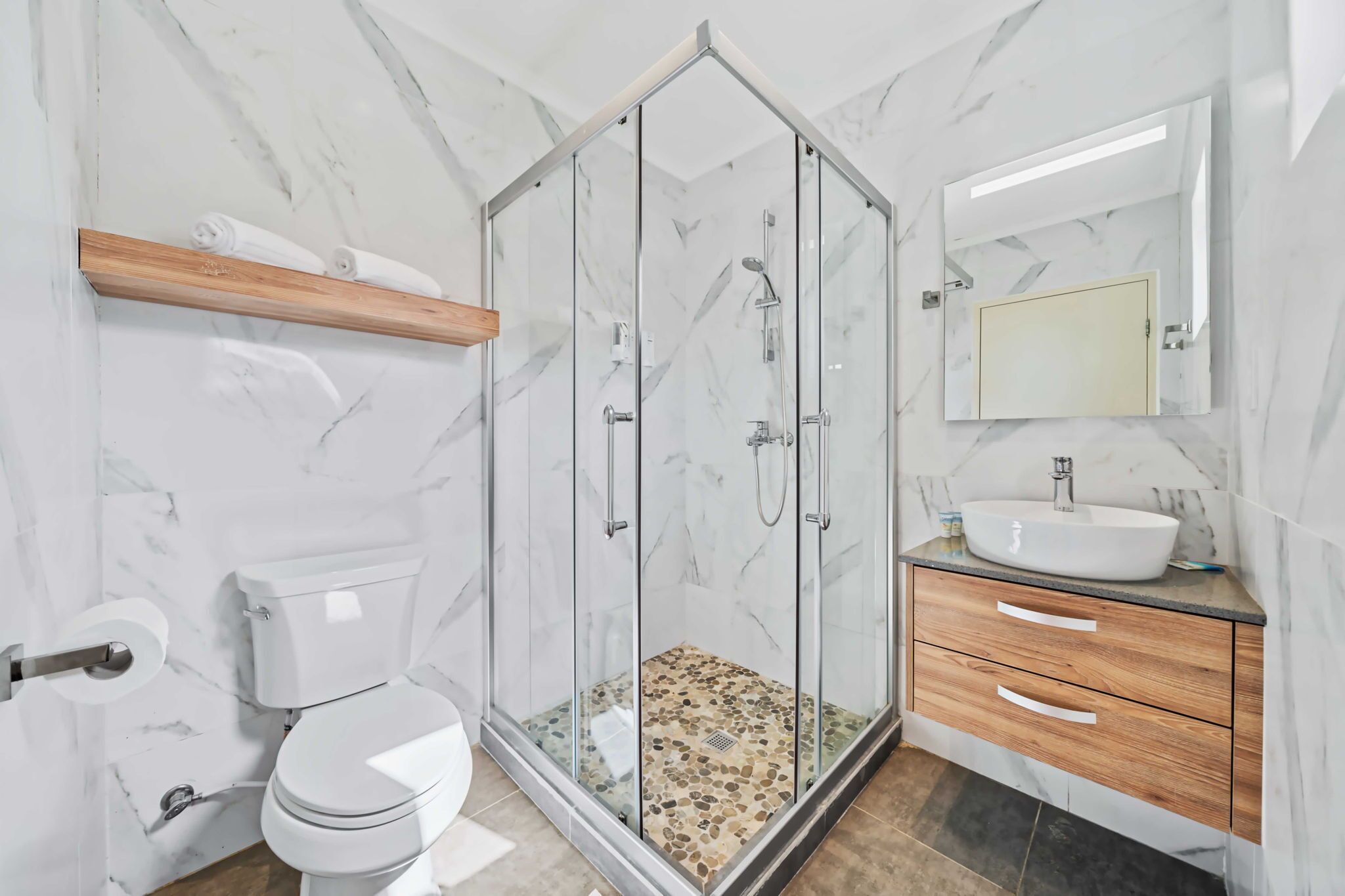 A modern bathroom with a glass-enclosed shower, a toilet, a sink with a mirror above, and wooden cabinets.