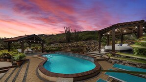 A swimming pool with a curved edge, surrounded by lounge chairs and a covered seating area. - Caya Mesa Vista 8 Tierra del Sol (Noord)