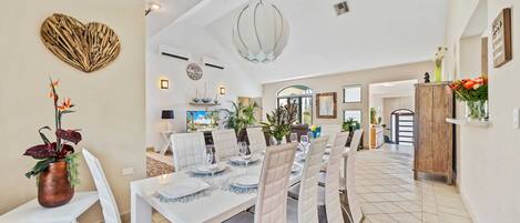 Une salle à manger spacieuse avec un plafond haut, des murs blancs et un grand lustre.
