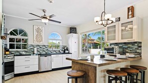 A modern kitchen with white cabinetry, a central island with stools, a ceiling fan, and a view of the outdoors.