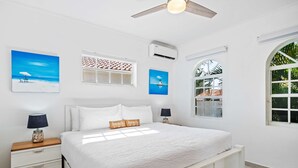 A bedroom with a bed, two nightstands, a ceiling fan, and a window with a view of palm trees.