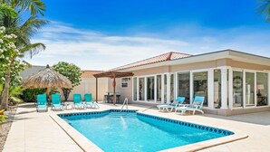 A swimming pool with lounge chairs, a covered patio, and a building with large windows.