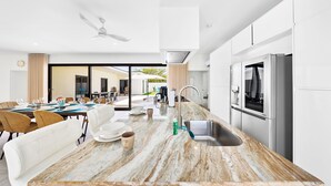 A modern kitchen with a marble countertop, stainless steel appliances, and a dining area with a white sofa and table. - Koyari 35-f (Noord)