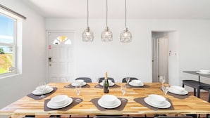 A dining area with a wooden table set for six, three hanging pendant lights, and a bottle of champagne. - Tibushi 1 (Noord)