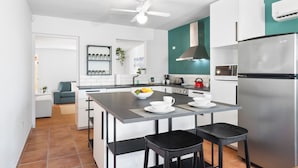A modern kitchen with a central island, white cabinets, a stainless steel refrigerator, and a teal accent wall. - Tibushi 1 (Noord)