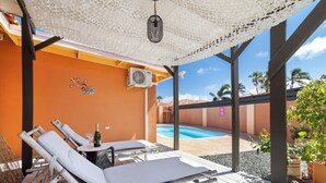 A poolside area with lounge chairs, a table with a bottle, and a view of a swimming pool. - Tibushi 1 (Noord)