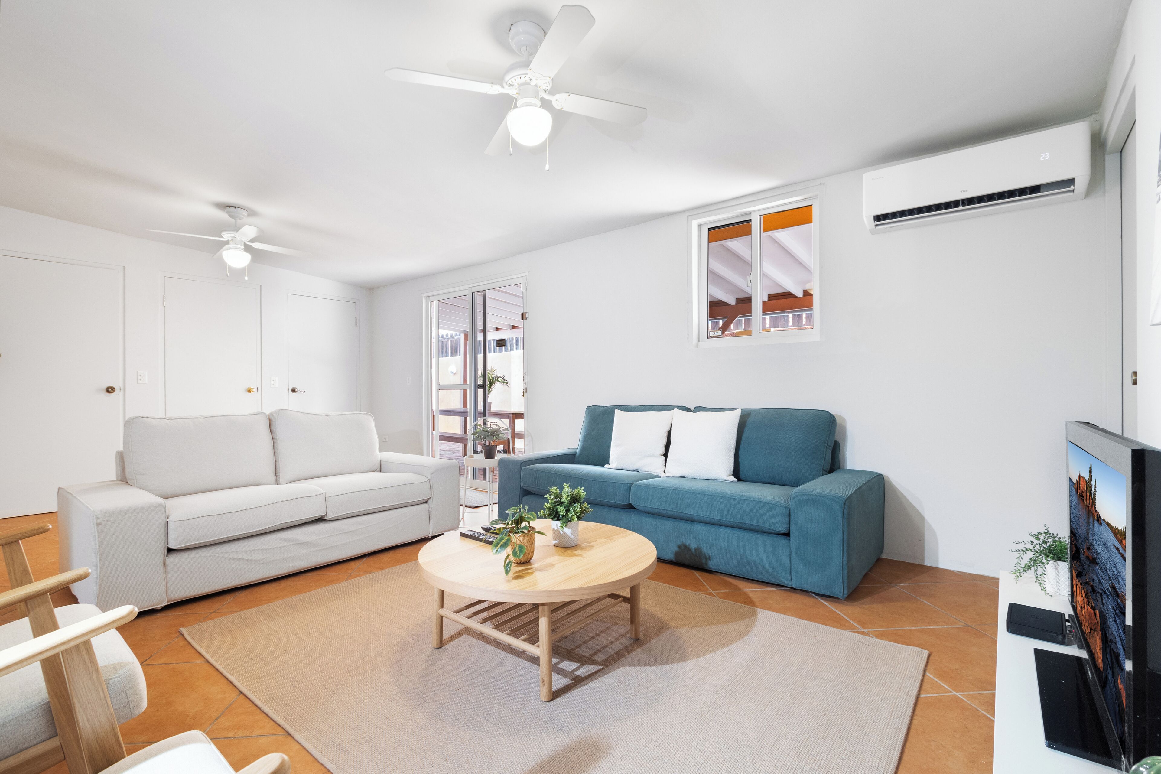 Un soggiorno moderno con un divano bianco, un divano blu, un tavolino in legno e una ventola a soffitto.