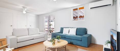 Un soggiorno moderno con un divano bianco, un divano blu, un tavolino in legno e una ventola a soffitto.