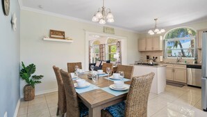 A dining area with a wooden table set for six, surrounded by wicker chairs. There is a kitchen area with stainless steel appliances and a window with a view of greenery. - Washington 41-n (Noord)