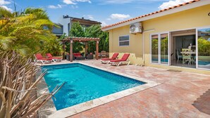 A swimming pool with red lounge chairs, a pergola, and a covered patio area. - Washington 41-n (Noord)
