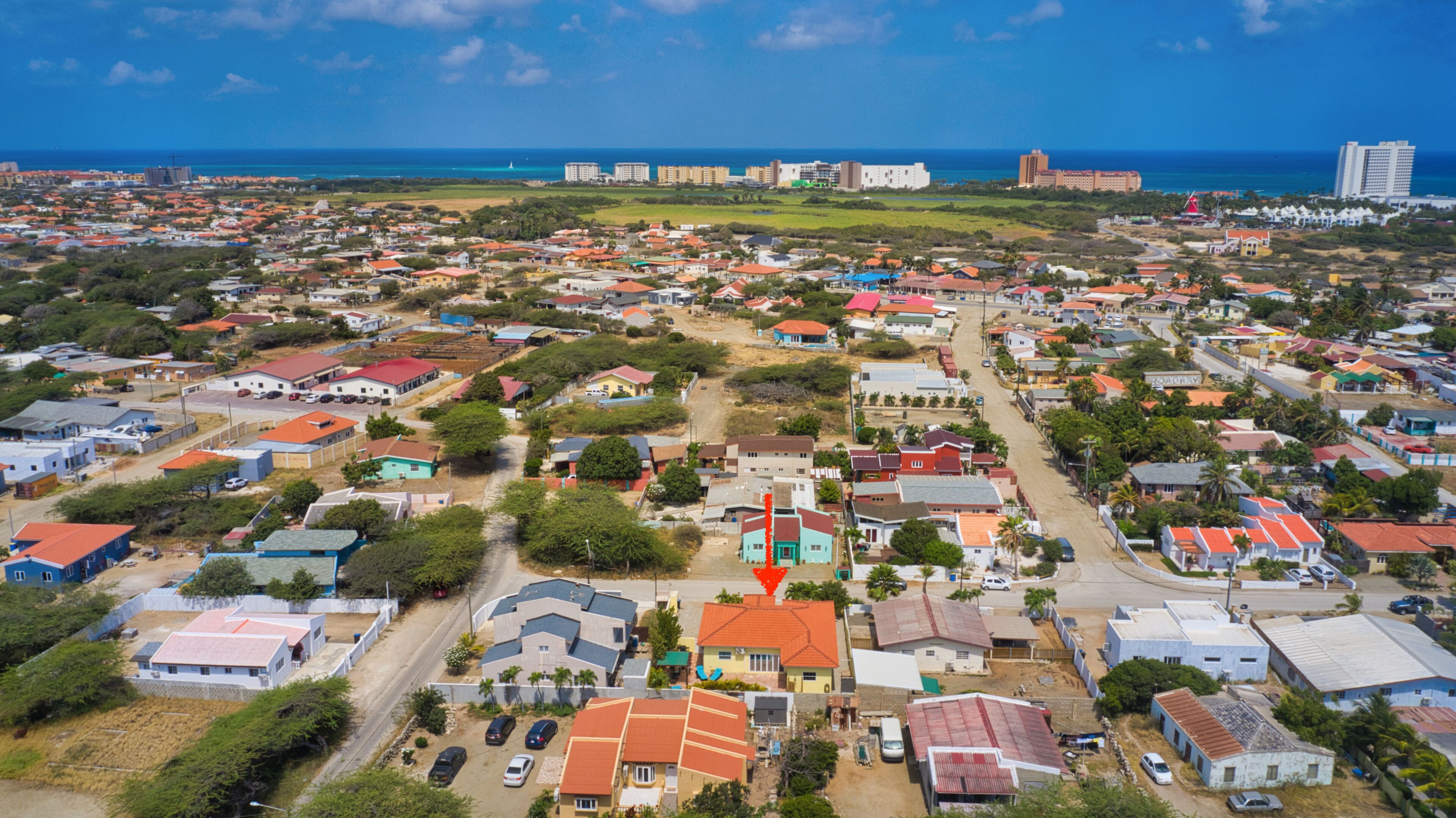 An aerial view of a residential area with houses, roads, and a distant view of the ocean.