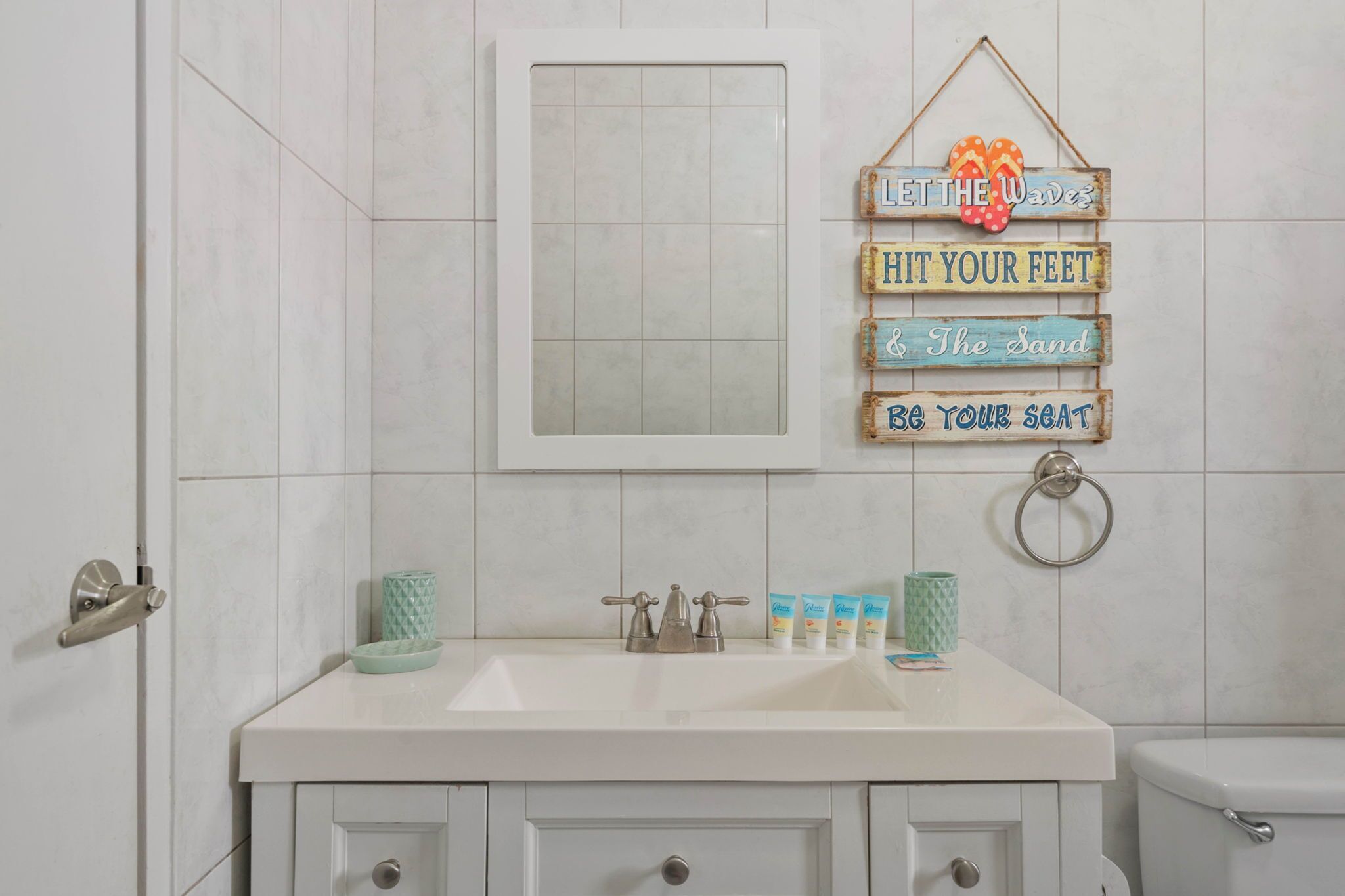 Une salle de bain avec un lavabo blanc, un miroir et des toilettes. Un panneau est fixé au mur, sur lequel on peut lire les inscriptions « Laissez la vague vous emporter » et « Sentez la puissance de la vague ».