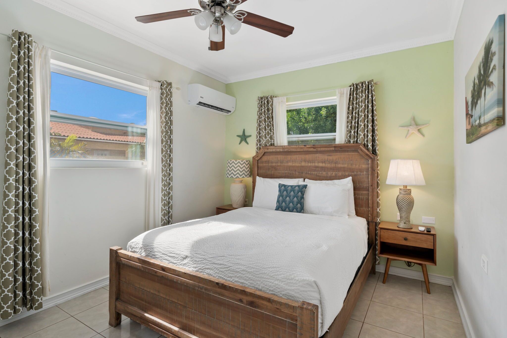 A bedroom with a wooden bed, a ceiling fan, a nightstand with a lamp, and a window with curtains.