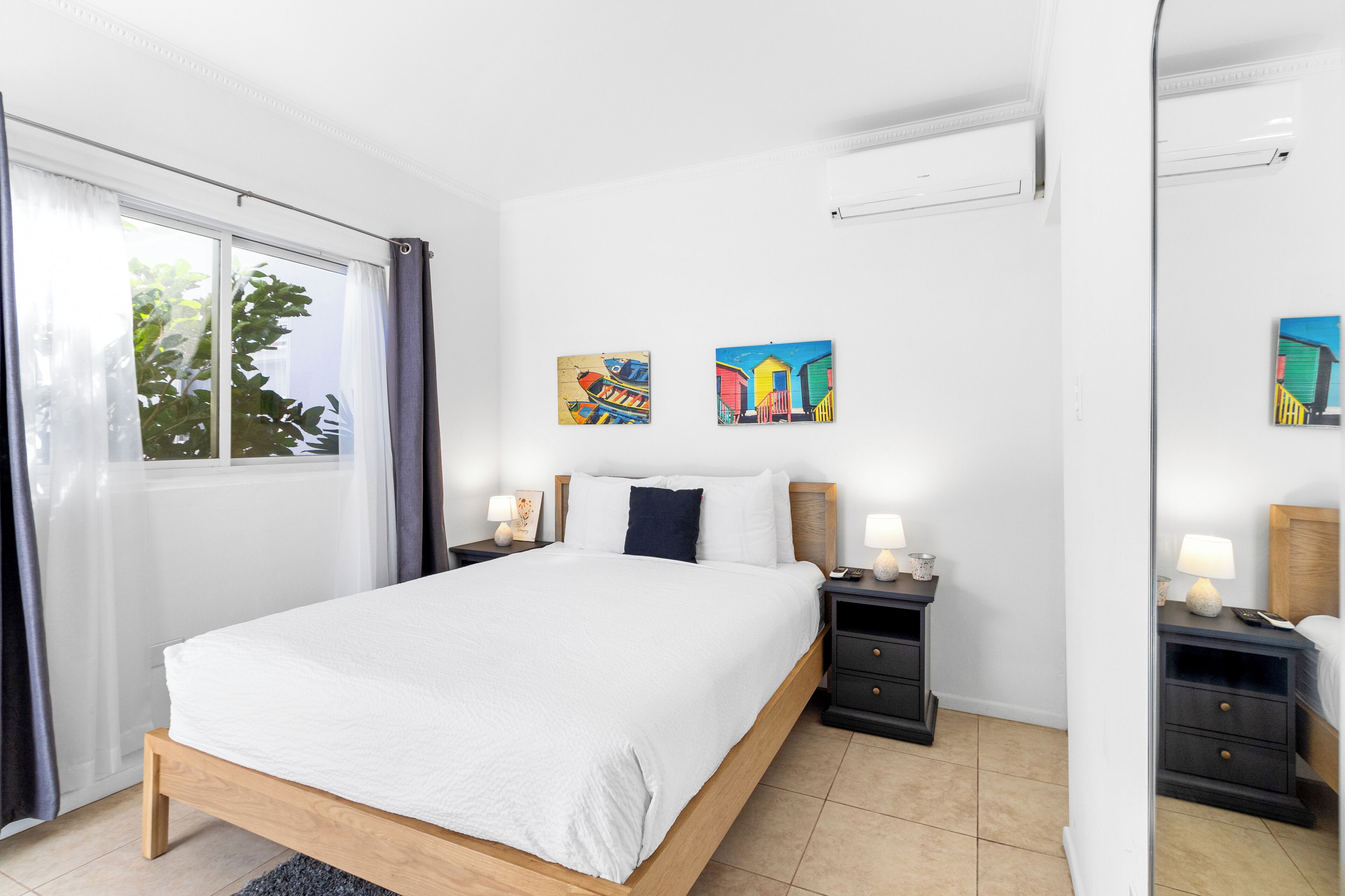 A bedroom with a large bed, two bedside tables, a mirror, and artwork on the wall.