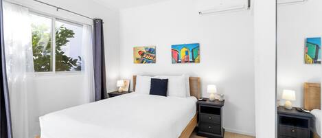 A bedroom with a large bed, two bedside tables, a mirror, and artwork on the wall.