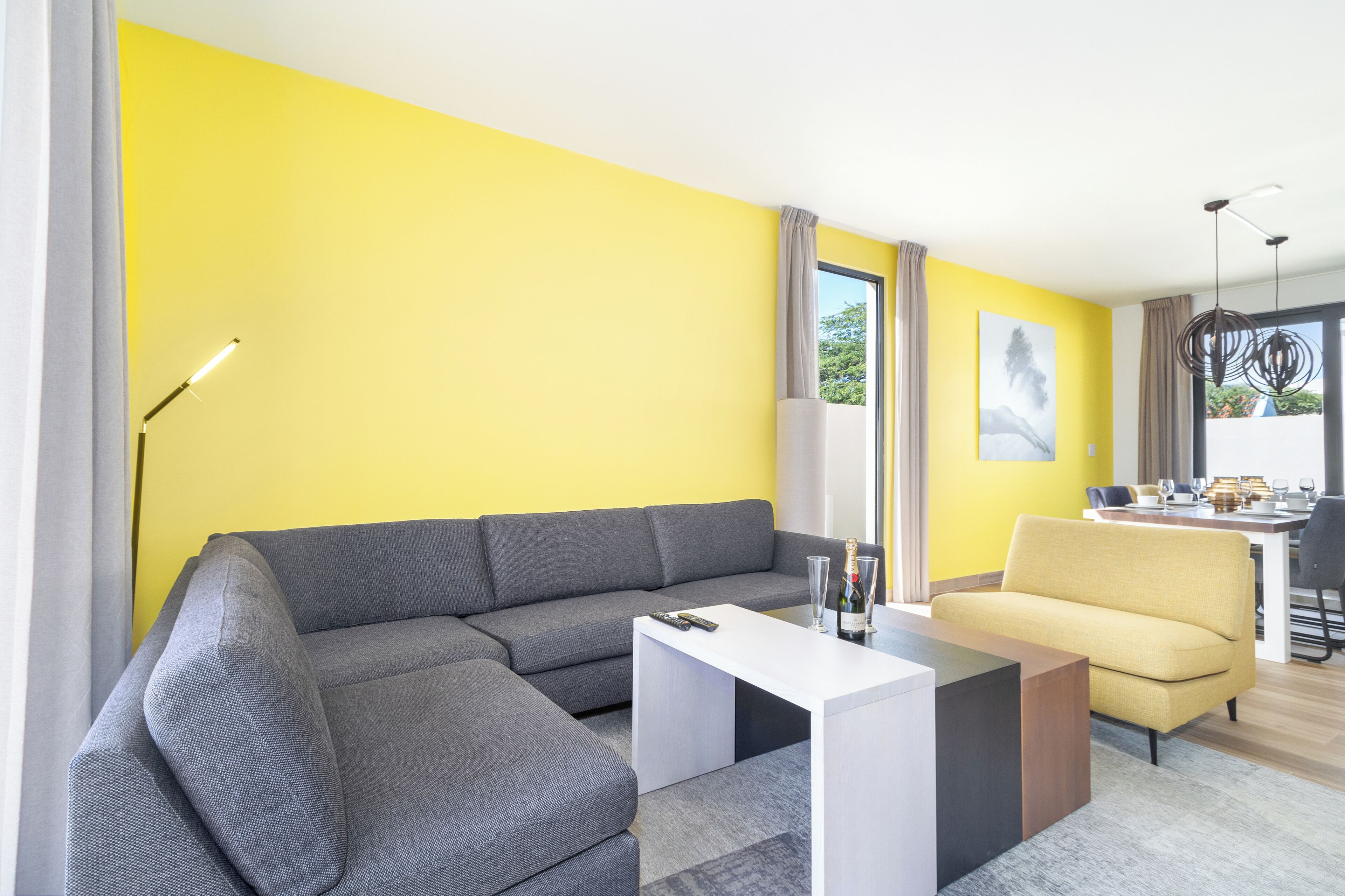 Een moderne woonkamer met een grijze modulaire bank, een witte salontafel en een gele fauteuil.