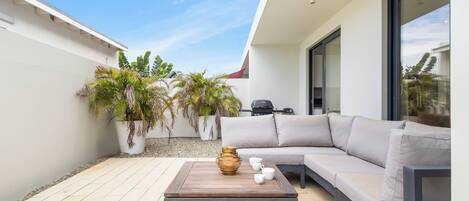 A modern outdoor patio with a wooden table, a grey sofa, and potted plants.