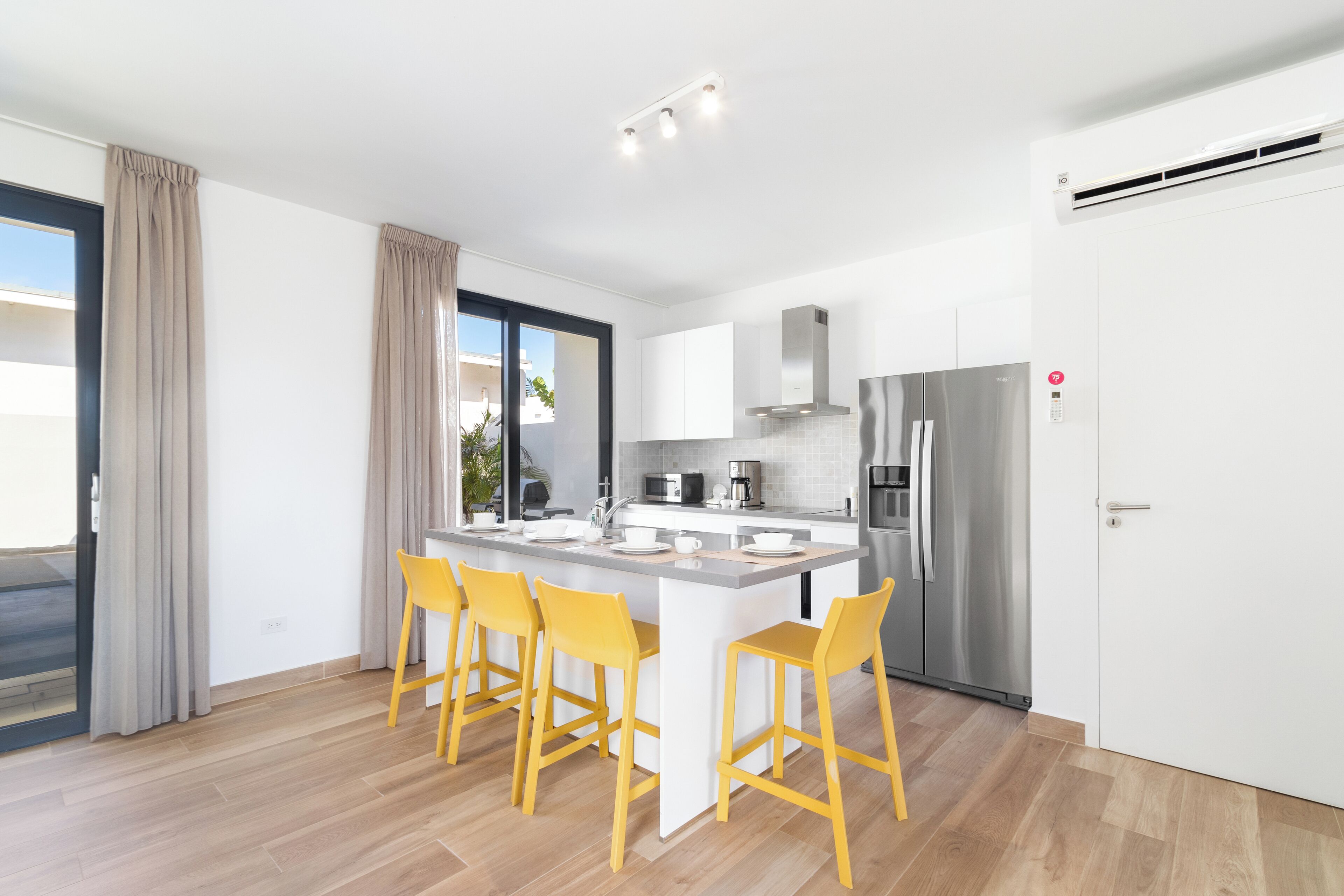 A modern kitchen with a central island, stainless steel appliances, and yellow bar stools.