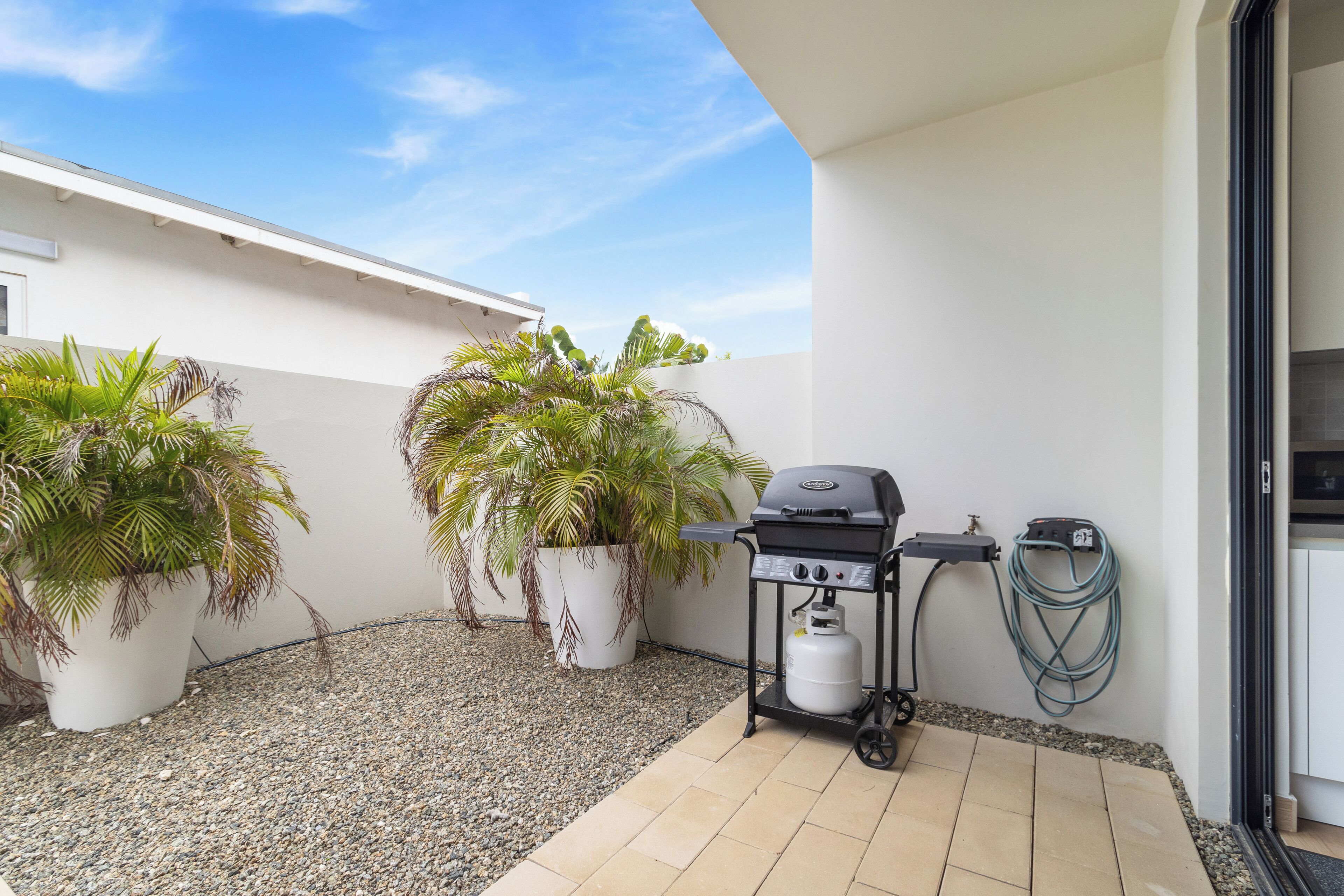 A patio with a grill, potted plants, and a hose.