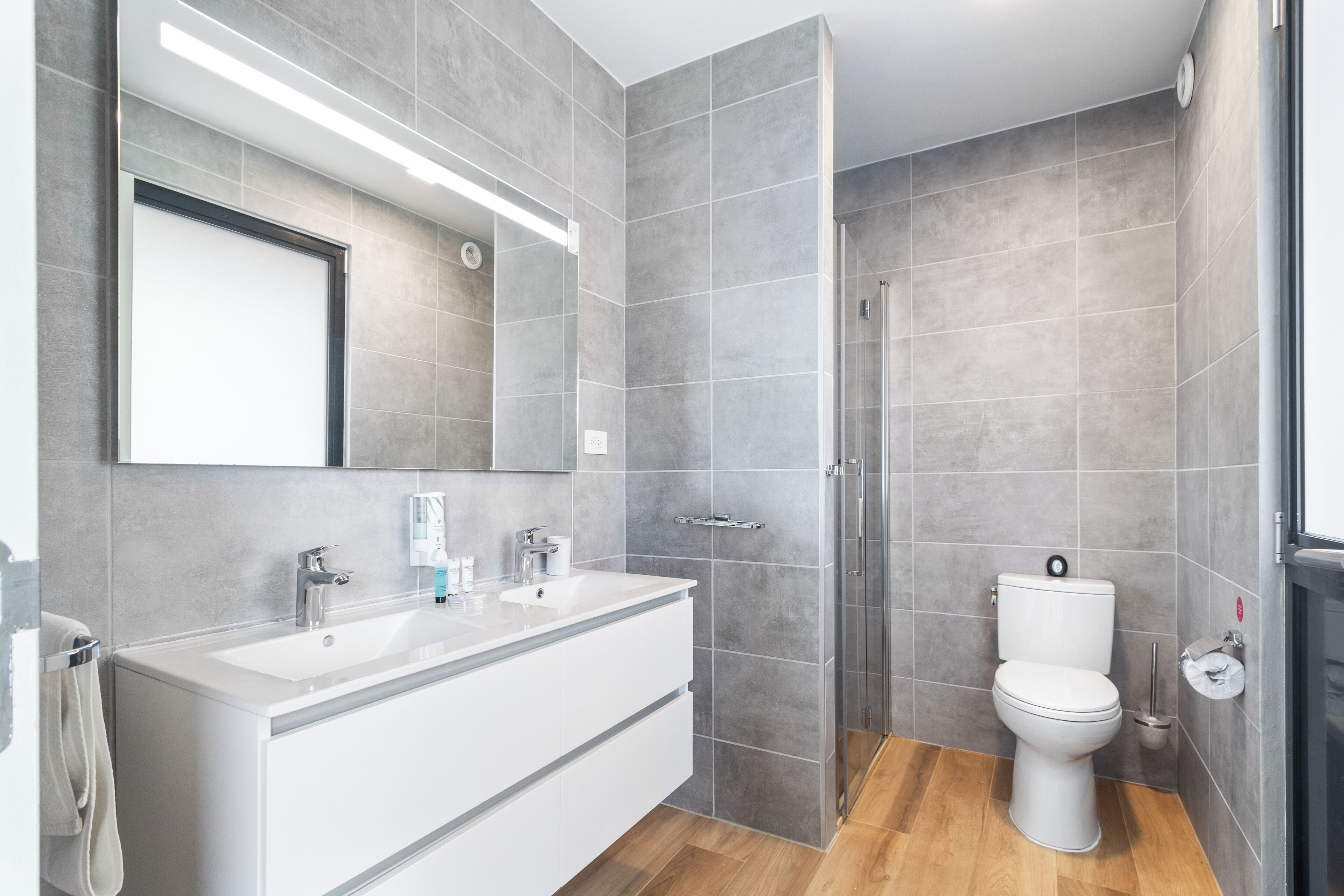 A modern bathroom with a large mirror, a white vanity, a toilet, and a shower area.
