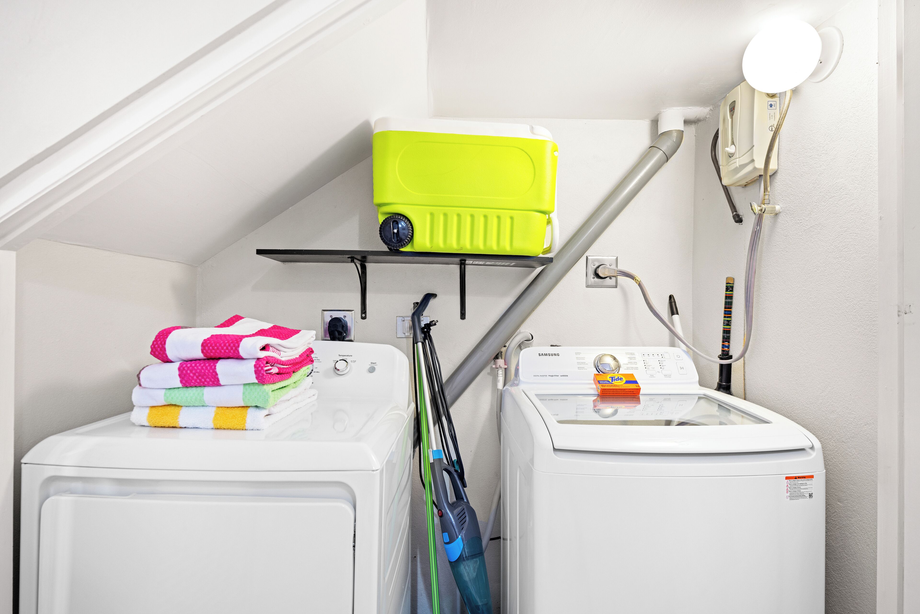 A laundry area with a washing machine, a dryer, and a green suitcase on a shelf.