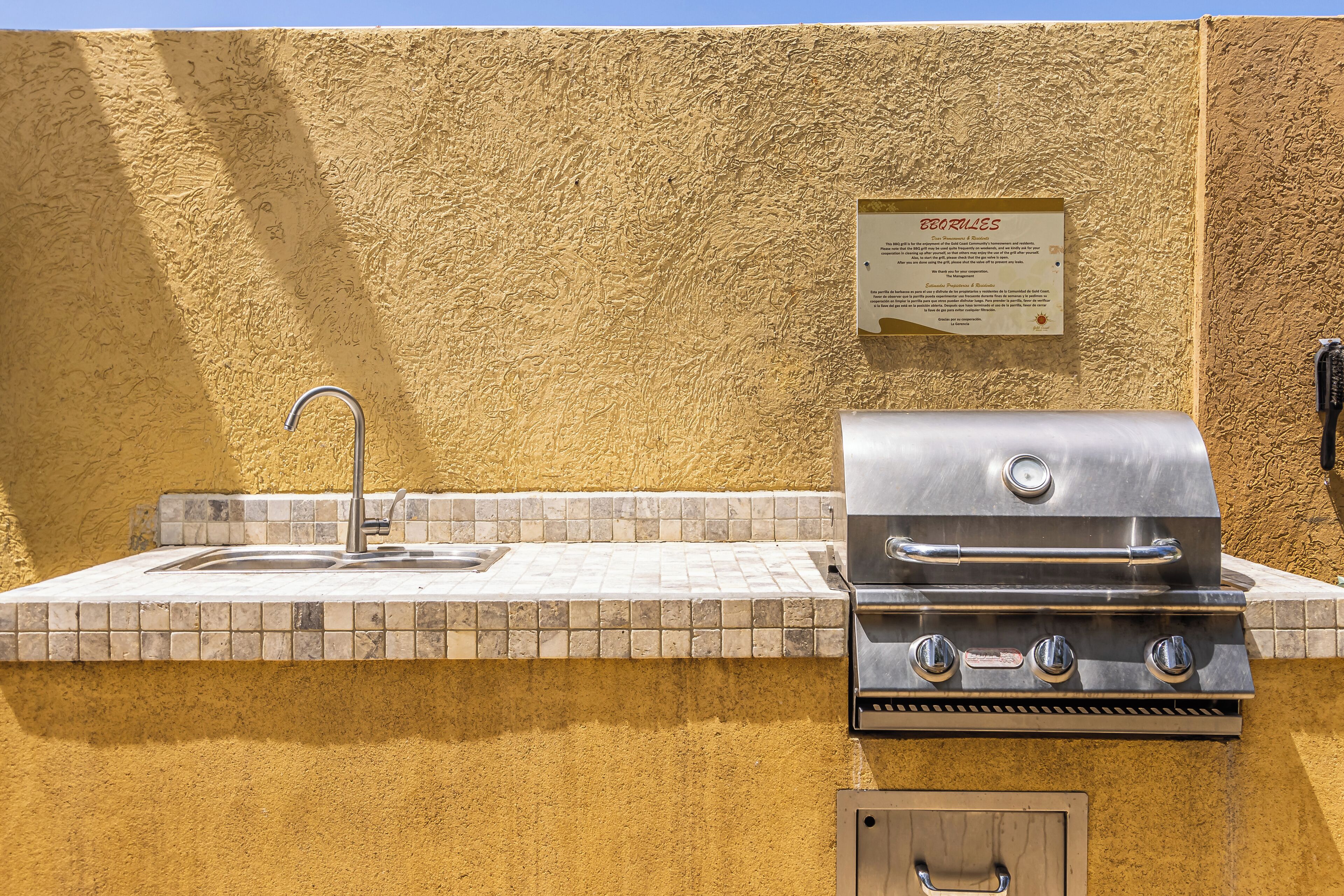 An outdoor kitchen with a sink and grill, a wall-mounted sign, and a tiled backsplash.