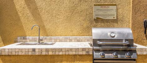 An outdoor kitchen with a sink and grill, a wall-mounted sign, and a tiled backsplash.