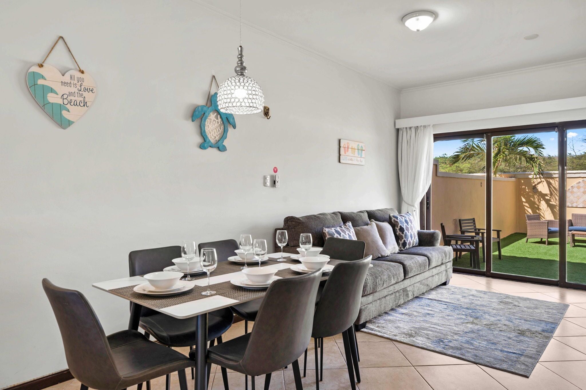 A dining area with a table set for four, a sofa with cushions, and a view of a patio with outdoor furniture.