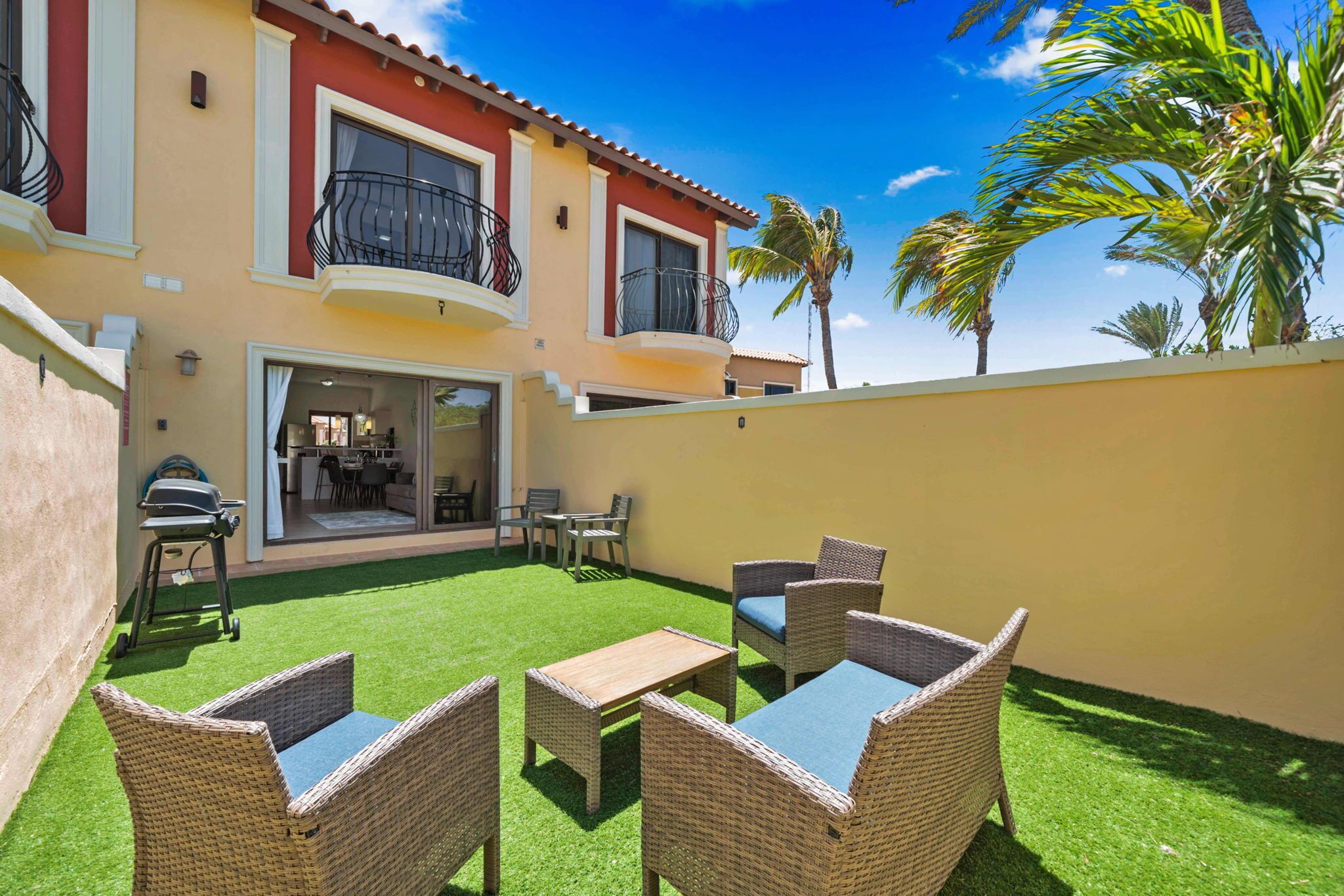 Une maison à deux étages avec un balcon, une terrasse dotée de meubles en osier et une pelouse.