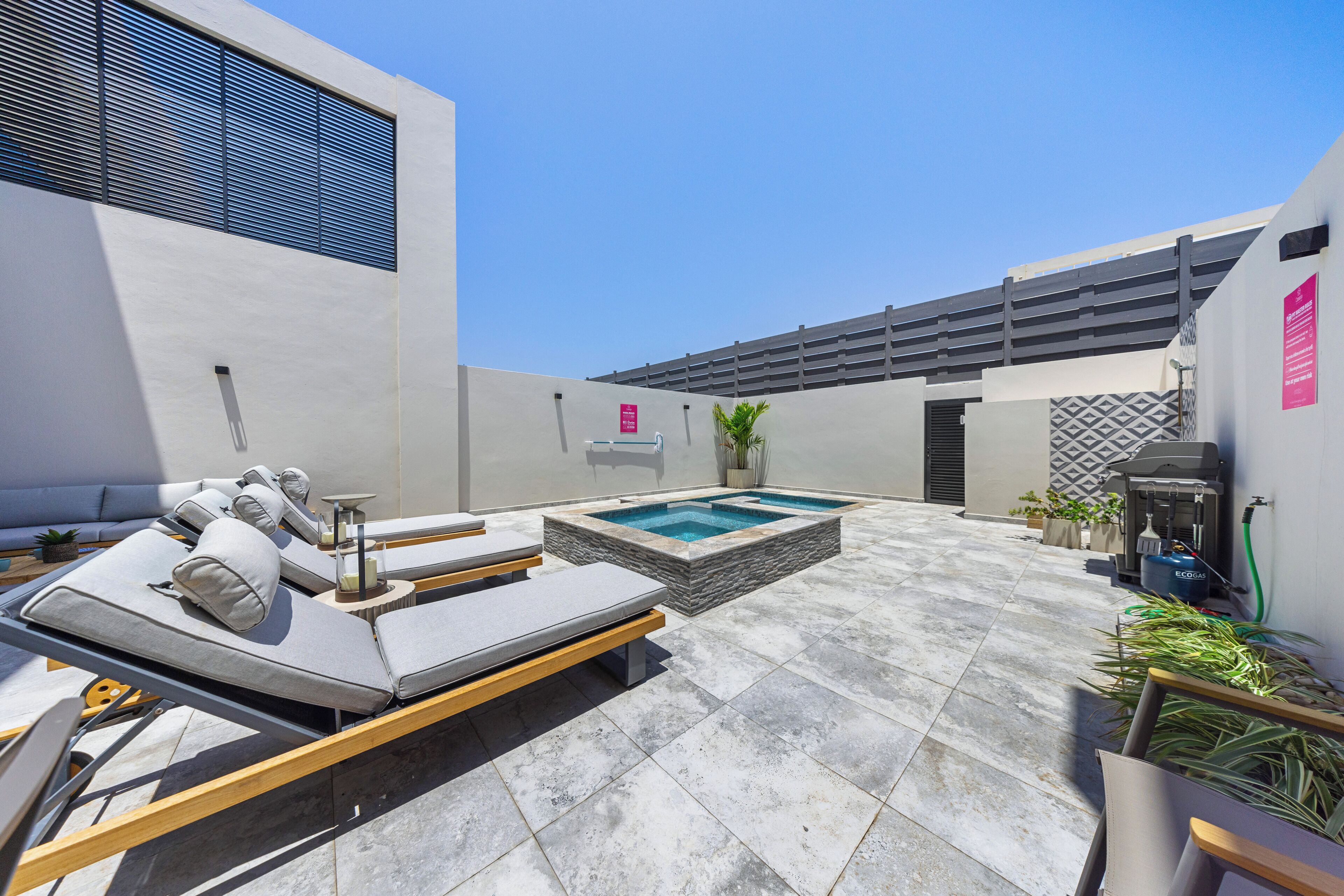 A modern outdoor patio with a pool, lounge chairs, and a barbecue area.