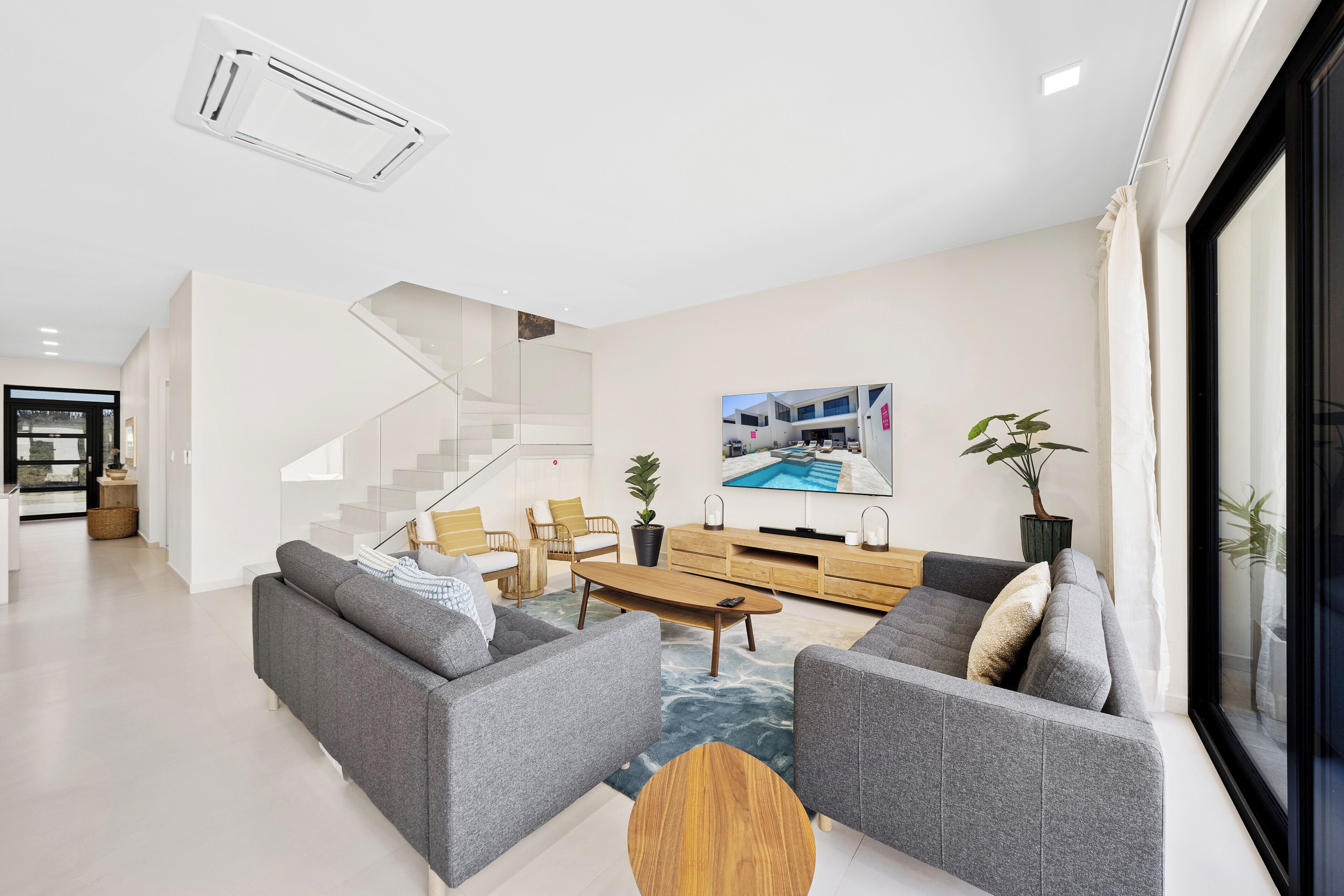 Een moderne woonkamer met grijze banken, een houten salontafel en een trap naar een hoger niveau.