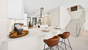 A modern kitchen with a central island, bar stools, and a staircase leading to an upper level. - Catalina Residence Apt 3 - L.g. Smith Boulevard 546-j (Noord)