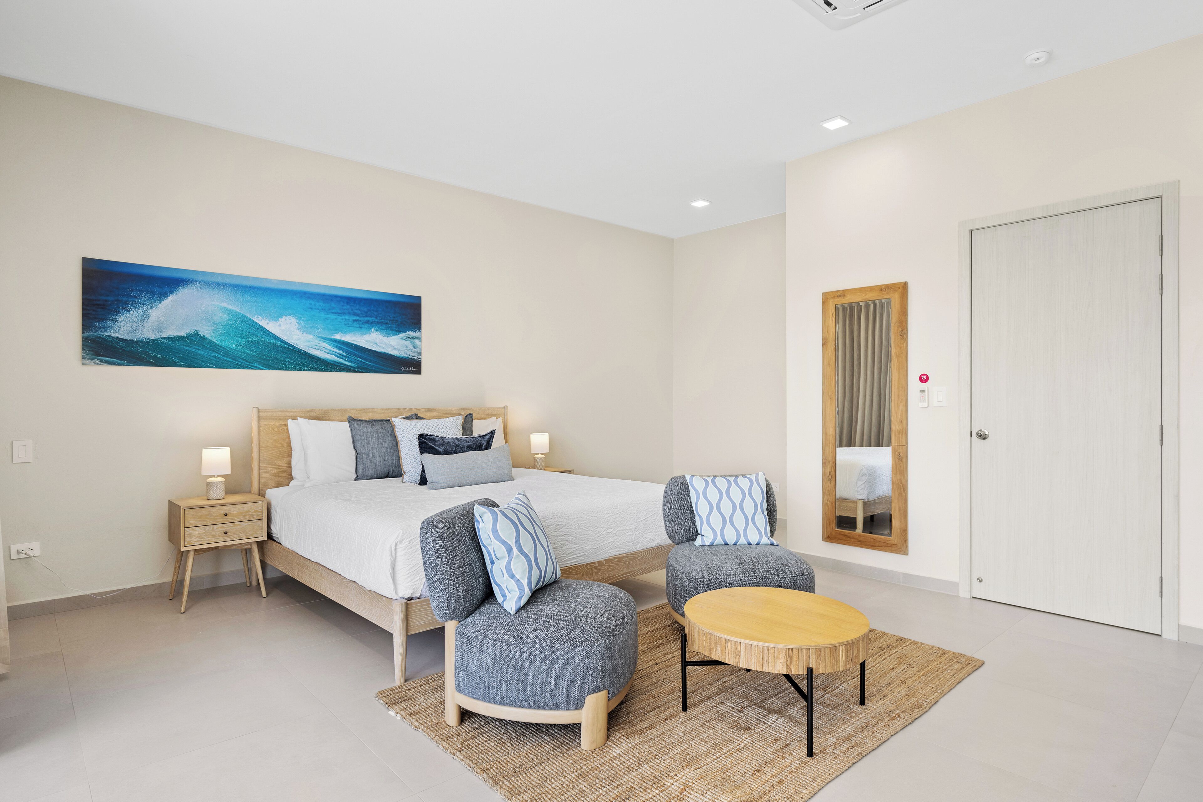 A modern hotel room with a large bed, two armchairs, a small table, and a painting of a wave on the wall.