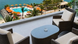 Ein Balkon mit Korbmöbeln, einem Glastisch und Blick auf Pool und Strand.