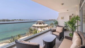 Ein Balkon mit Korbmöbeln, Blick auf das Meer und ein Gebäude gegenüber.