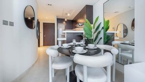 A modern dining area with a round table set for four, white upholstered chairs, and a large mirror on the wall. - StayShort - Sky Gardens Studio with Skyscraper Views in DIFC! (DIFC)
